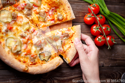 Image of Hand picking tasty slice of pizza lying on wooden table