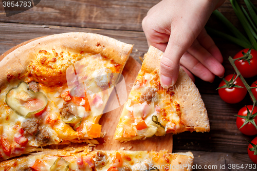 Image of Hand picking tasty slice of pizza lying on wooden table