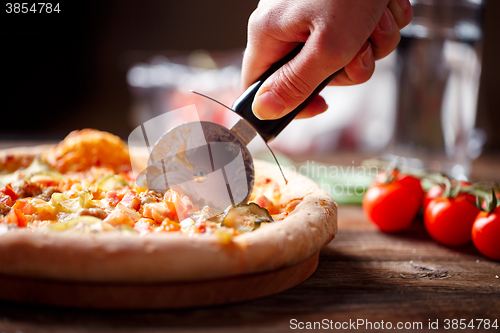 Image of Slicing fresh pizza with roller knife. 