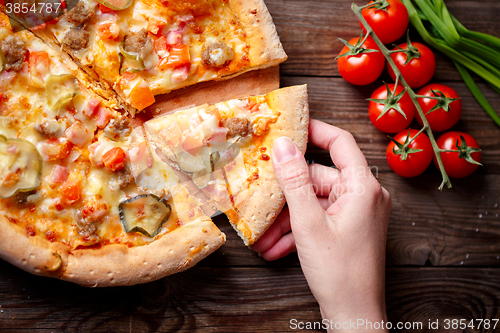 Image of Hand picking tasty slice of pizza lying on wooden table