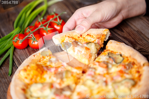 Image of Hand picking tasty slice of pizza lying on wooden table