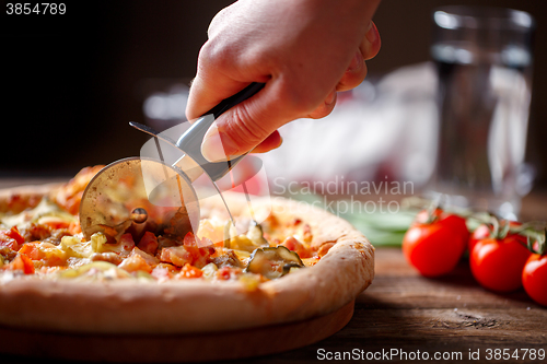 Image of Slicing fresh pizza with roller knife. 