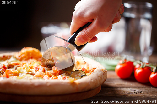 Image of Slicing fresh pizza with roller knife. 