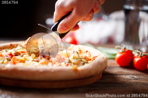 Image of Slicing fresh pizza with roller knife. 