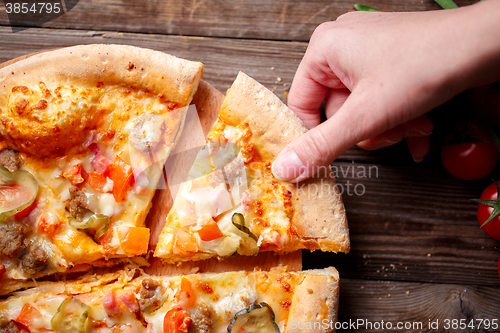 Image of Hand picking tasty slice of pizza lying on wooden table