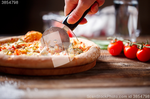 Image of Slicing fresh pizza with roller knife. 