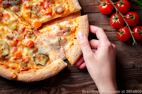 Image of Hand picking tasty slice of pizza lying on wooden table