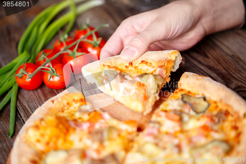 Image of Hand picking tasty slice of pizza lying on wooden table