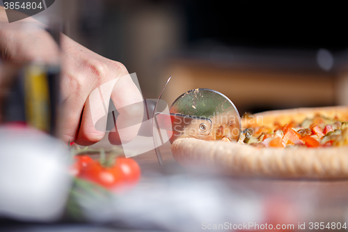 Image of Slicing fresh pizza with roller knife. 