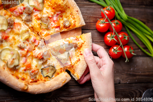 Image of Hand picking tasty slice of pizza lying on wooden table