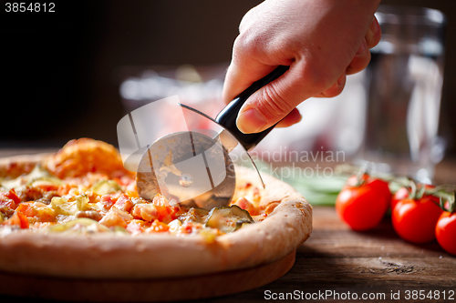 Image of Slicing fresh pizza with roller knife. 