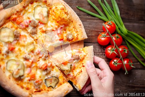 Image of Hand picking tasty slice of pizza lying on wooden table