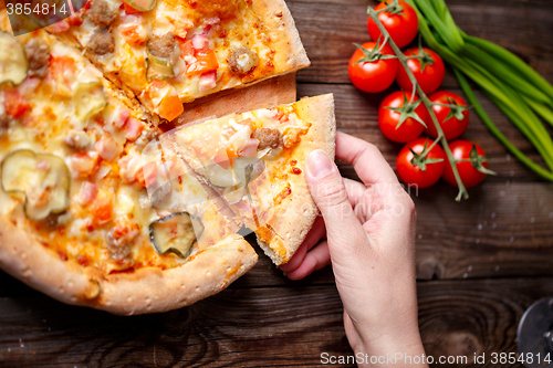 Image of Hand picking tasty slice of pizza lying on wooden table