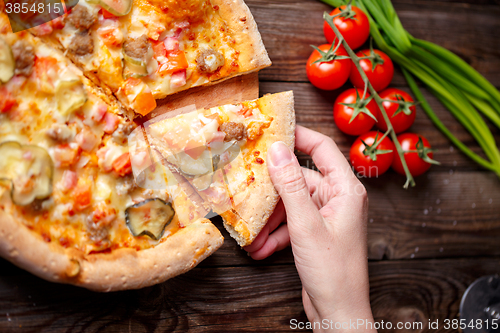 Image of Hand picking tasty slice of pizza lying on wooden table