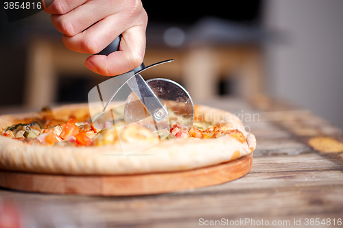 Image of Slicing fresh pizza with roller knife. 