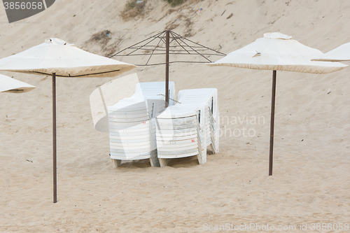 Image of Two stacks of folded chairs on the beach with umbrellas