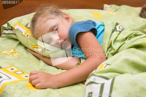 Image of Little girl sleeping on her side in bed with his hand under the pillow and covered with a blanket