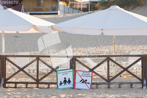Image of Anapa, Russia - September 21, 2015: Signs a - place children bathing, storm, swimming prohibited - lie on the sandy beach near the fence with a parasol
