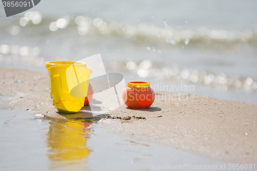 Image of Childrens toy dishes items left on the sandy shore by the water