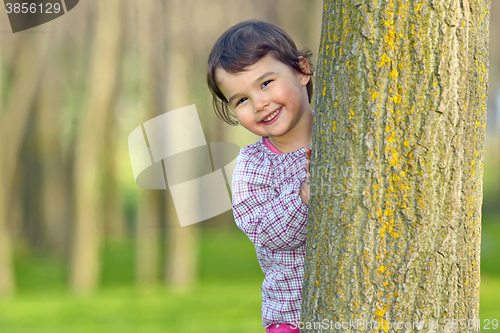 Image of Little girl hiding behind a tree