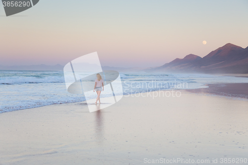 Image of Lady walking on sandy beach in sunset.