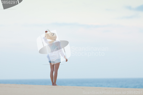 Image of Woman on sandy beach in white shirt in morning. 