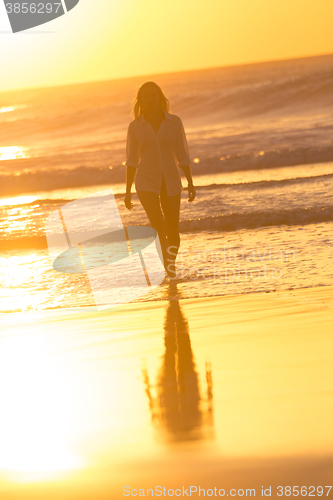 Image of Lady walking on sandy beach in sunset.