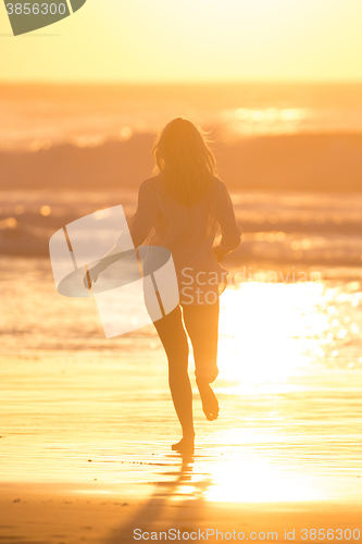 Image of Woman running on the beach in sunset.