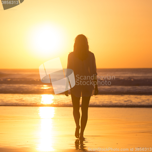 Image of Lady walking on sandy beach in sunset.