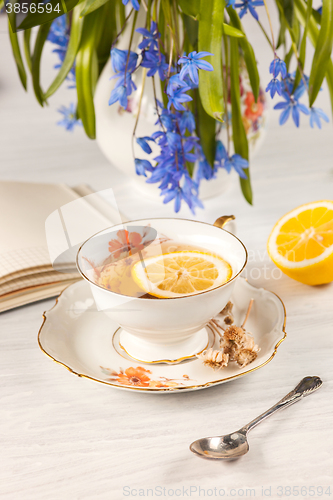 Image of Tea with  lemon and bouquet of  blue primroses on the table