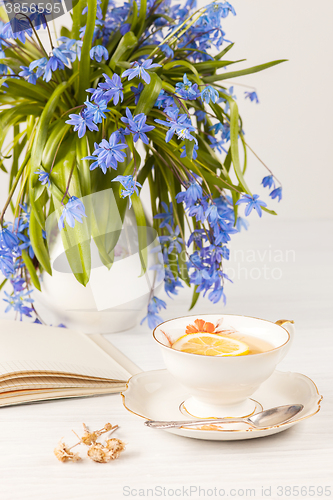 Image of Tea with  lemon and bouquet of  blue primroses on the table