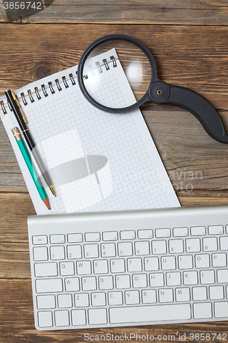 Image of computer keyboard, ballpoint pen, pencil, notepad and magnifying