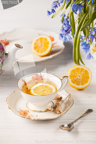 Image of Tea with  lemon and bouquet of  blue primroses on the table