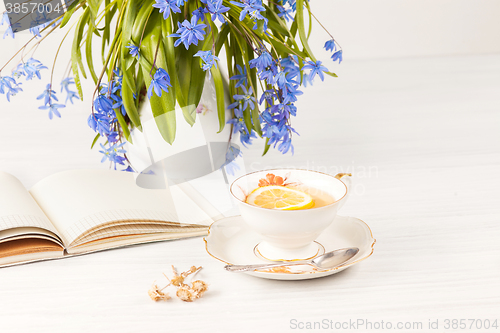 Image of Tea with  lemon and bouquet of  blue primroses on the table