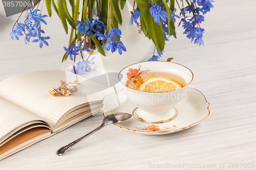 Image of Tea with  lemon and bouquet of  blue primroses on the table