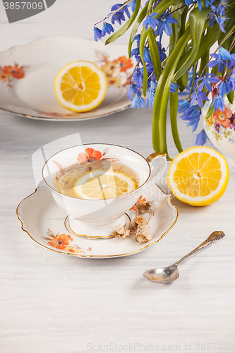 Image of Tea with  lemon and bouquet of  blue primroses on the table