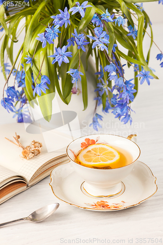 Image of Tea with  lemon and bouquet of  blue primroses on the table