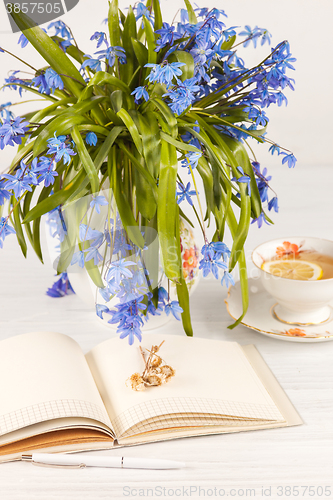 Image of Tea with  lemon and bouquet of  blue primroses on the table