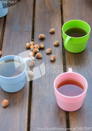 Image of Three multi-colored cups of tea on a wooden table hazelnuts and walnuts