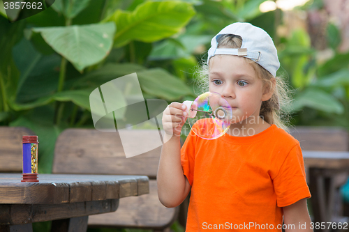 Image of  Little girl in a bright T-shirt inflates large bubble in the street