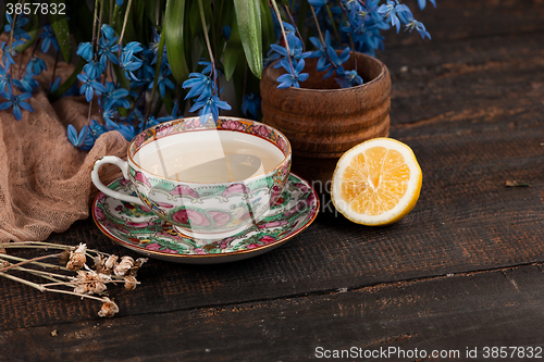 Image of Tea with  lemon and bouquet of  blue primroses on the table