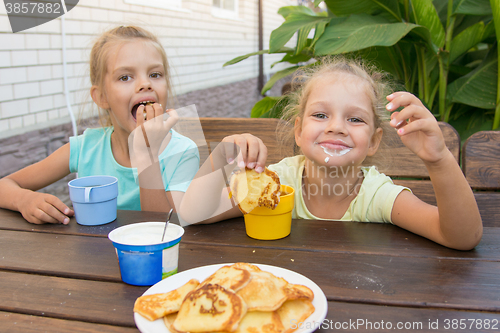 Image of Satisfied children at a table in the courtyard eating pancakes with sour cream