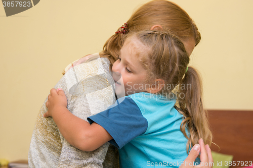 Image of The four-year daughter hugging her mother sitting on the bed in the room