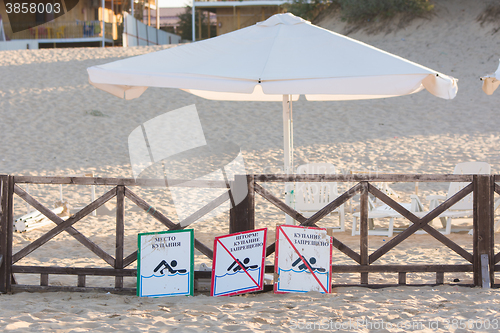 Image of Anapa, Russia - September 21, 2015: Signs a - place children bathing, storm, swimming prohibited - lie on the sandy beach near the fence with a parasol