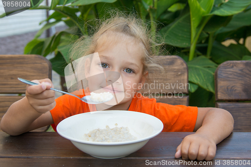 Image of Little girl smiling at a wooden table on a background of green eating porridge
