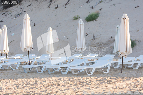 Image of Rows of empty chairs on the beach with a deflated parasols