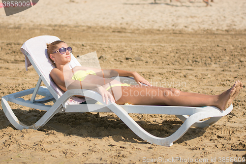 Image of Young slim tanned girl sunbathes on a beach lounger