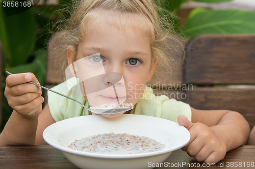 Image of Four-year-girl at the table in the fresh air blowing on a spoonful of porridge