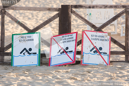 Image of Anapa, Russia - September 21, 2015: Signs - bathing place, storm, swimming prohibited and swimming forbidden - lie on the sandy beach near the fence with a parasol