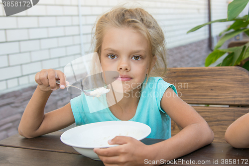 Image of Six year old girl at a wooden table in the yard eating porridge